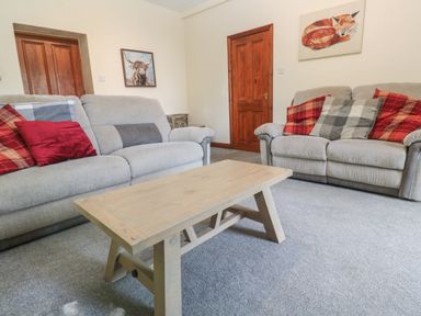 A living room with two grey sofas with red and grey cushions and a wooden coffee table at Beggars Roost in Penhallow