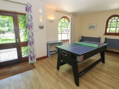 A game room with a ping pong table benches a small table and windows at Beggars Roost in Penhallow
