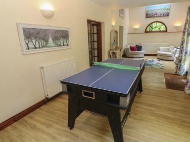 A room with a ping pong table in the foreground and two armchairs with cushions in the background at Beggars Roost in Penhallow