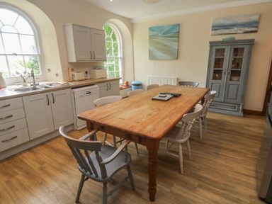 A kitchen with a wooden dining table and chairs near grey cabinets and a window at Beggars Roost in Penhallow