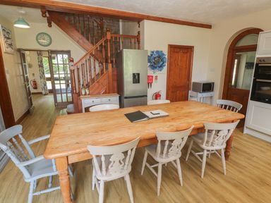 A dining area with a wooden table and six chairs near a staircase and refrigerator at Beggars Roost in Penhallow