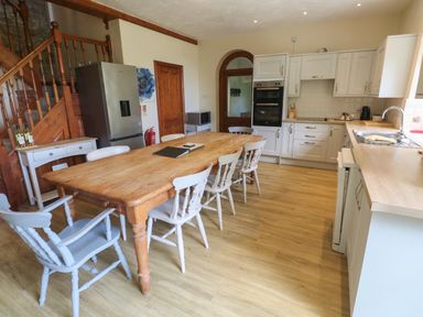 A kitchen with a wooden dining table surrounded by chairs and white cabinets at Beggars Roost in Penhallow