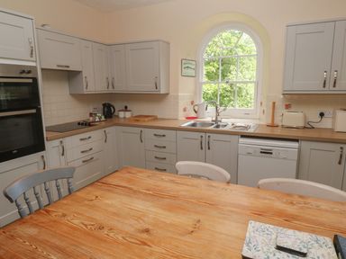 A kitchen with gray cabinets wooden countertop a wooden table and arched window at Beggars Roost in Penhallow