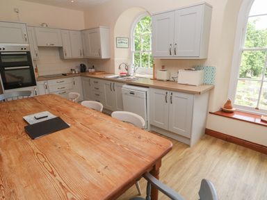 A kitchen with wooden table and chairs dishwasher ovens and windows showing greenery at Beggars Roost in Penhallow