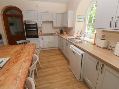 A kitchen with a wooden table and chairs grey cabinets a dishwasher and a window at Beggars Roost in Penhallow