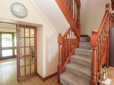 A wooden staircase with carpeted steps and a round clock on the wall near a glass-panel door at Beggars Roost in Penhallow
