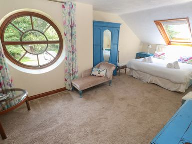 A bedroom with a round window chaise lounge blue wardrobe and bed at Beggars Roost in Penhallow
