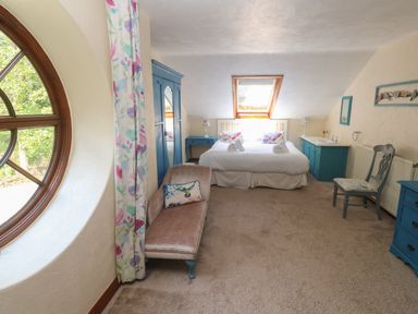A bedroom with a double bed two blue dressers a blue wardrobe a chair and a window at Beggars Roost in Penhallow