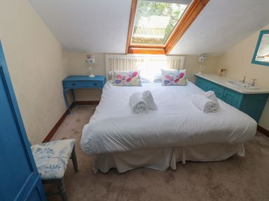 A bedroom with a double bed white bedding and floral pillows under a skylight window at Beggars Roost in Penhallow