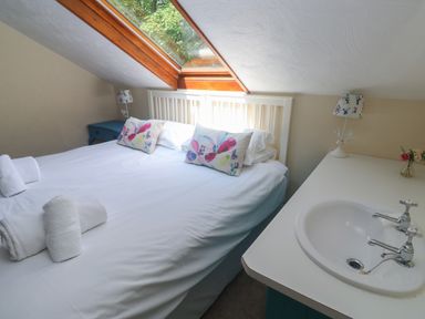 A bedroom with a bed with floral pillows a skylight window and a sink on a countertop at Beggars Roost in Penhallow