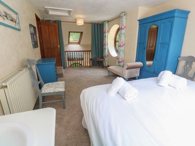 A bedroom with a bed with rolled towels bedside chairs a blue wardrobe and a window with curtains at Beggars Roost in Penhallow