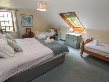 A bedroom with a double bed and two single beds a chest of drawers a window and a skylight window at Beggars Roost in Penhallow