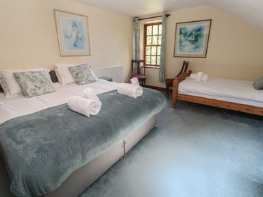 A bedroom with a double bed and a single bed with rolled towels and two chairs near a window at Beggars Roost in Penhallow