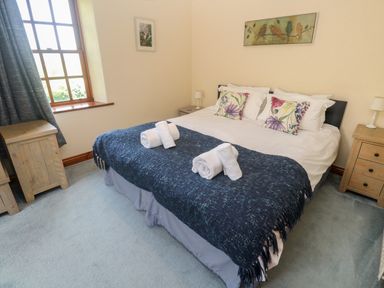 A bedroom with a double bed pillows with floral covers bedside tables lamps and a window at Beggars Roost in Penhallow