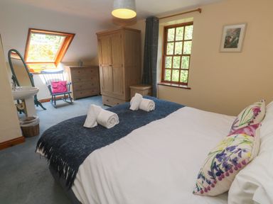 A bedroom with a bed two rolled towels wardrobe chest of drawers rocking chair and a sink at Beggars Roost in Penhallow