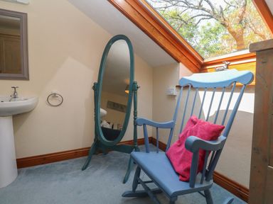 A room with a blue rocking chair with a red cushion a free standing oval mirror a sink and a skylight window at Beggars Roost in Penhallow