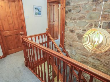 A staircase with wooden railings next to a stone wall and a hanging light at Beggars Roost in Penhallow