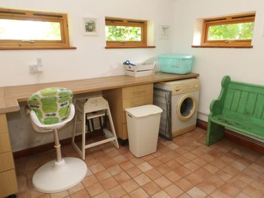 A utility room with a washing machine a green bench a high chair and a laundry basket at Beggars Roost in Penhallow