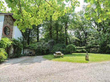 An outdoor area with a gravel path a wooden picnic table and green trees at Beggars Roost in Penhallow