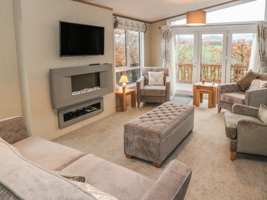 A living room with armchairs a sofa a wall-mounted tv and fireplace and a window showing an outdoor view at Avonal Lodge 24 in Dunning