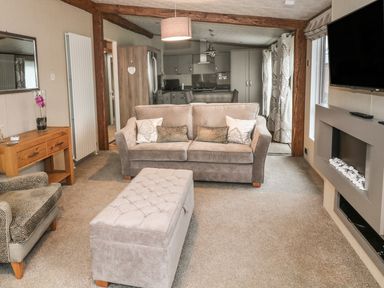 A living room with a sofa a chair an ottoman a wall-mounted TV and a wooden side table at Avonal Lodge 24 in Dunning