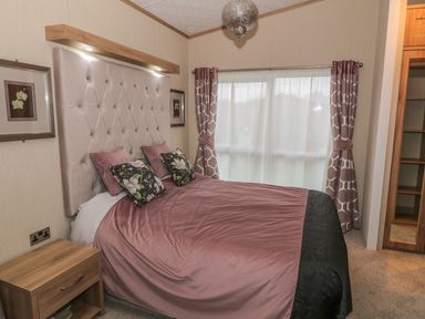 A bedroom with a bed with floral pillows a headboard nightstand window with curtains and a closet at Avonal Lodge in Dunning