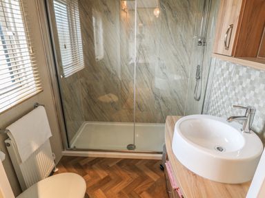 A bathroom with a shower, sink, toilet, and towel on radiator at Avonal Lodge (24) in Dunning