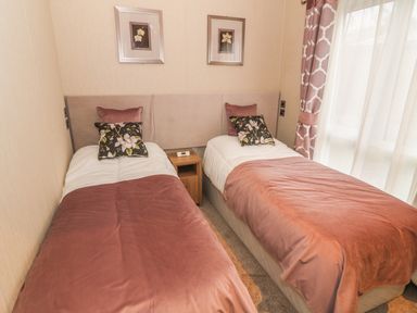 A bedroom with two single beds separated by a wooden nightstand and a window with patterned curtains at Avonal Lodge 24 in Dunning