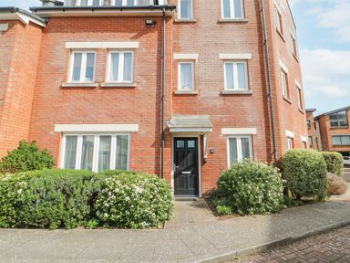 A brick apartment building with a black front door and white framed windows surrounded by bushes at Admirals Quarter Apartment 4 in Weymouth