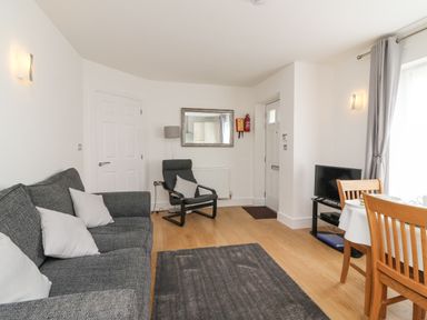 A living room with a grey sofa a black armchair a wooden dining table with chairs and a television at Admirals Quarter Apartment 4 in Weymouth