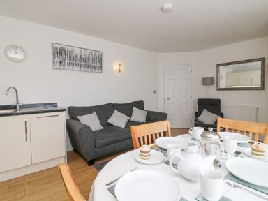 A dining table set with plates and cups next to a kitchen area and a living room with a sofa and armchair at Admiral's Quarter Apartment 4 Weymouth