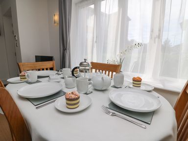 A dining table set with white plates, cups, and a teapot near a window with sheer curtains at Admiral's Quarter Apartment 4 in Weymouth