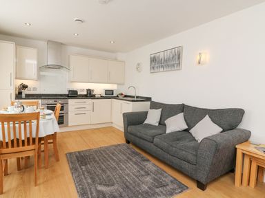 A kitchen and living area with a gray sofa white cabinets wooden dining table and chairs at Admirals Quarter Apartment 4 in Weymouth