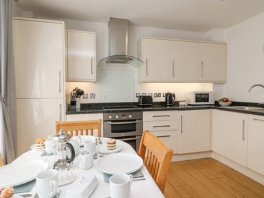 A kitchen with white cabinets wooden chairs and a table set for tea at Admiral's Quarter Apartment 4 in Weymouth