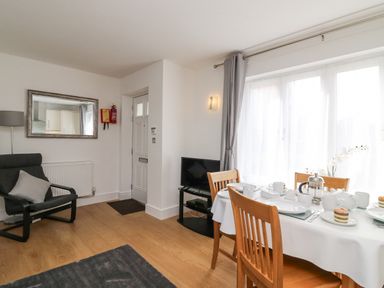 A dining area with a table set for tea and wooden chairs next to a window and a black armchair near a door at Admiral's Quarter Apartment 4 in Weymouth