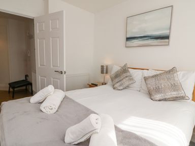 A bedroom with a double bed pillows bedside table with lamp and an open door at Admiral's Quarter Apartment 4 in Weymouth