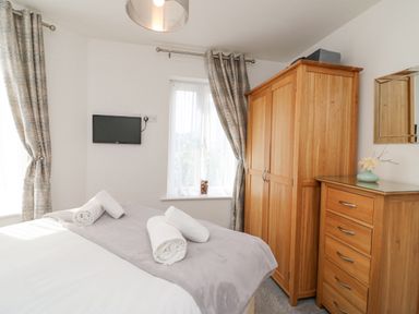 A bedroom with a bed towels on it wooden wardrobe chest of drawers and wall mounted TV at Admiral's Quarter Apartment 4 Weymouth