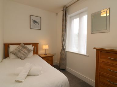 A bedroom with a single bed bedside table with lamp wooden chest of drawers window with curtains and a turtle picture on the wall at Admiral's Quarter Apartment 4 Weymouth