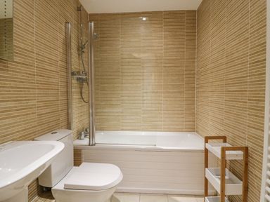 A bathroom with a bathtub shower toilet sink and a small shelving unit at Admirals Quarter Apartment 4 Weymouth
