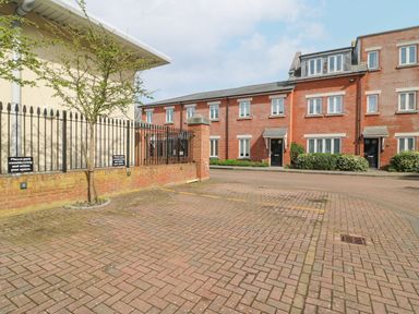 A brick paved parking area with numbered spaces near a brick apartment building with black doors at Admirals Quarter Apartment 4 in Weymouth