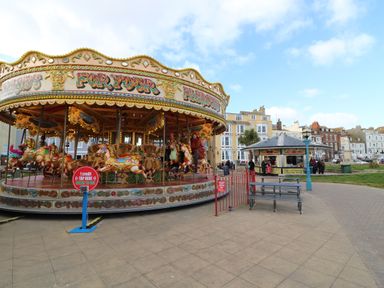A carousel with children riding horses near a food kiosk and seating area in an outdoor square at Admiral's Quarter Apartment 4 in Weymouth