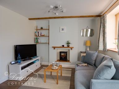A living room with a television on a white stand a gray sofa a small wooden coffee table and a fireplace at Ammonite Cottage Fortuneswell Portland