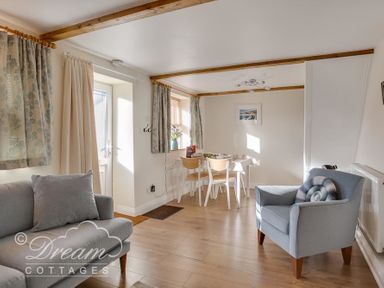 A sitting area with a sofa and armchair and a dining table with chairs near windows at Ammonite Cottage Fortuneswell Portland