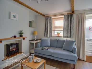 A sitting room with a blue sofa and coffee table near a window with curtains at Ammonite Cottage in Fortuneswell Portland