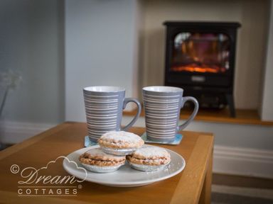Two striped mugs and three mince pies on a plate on a wooden table with a fireplace in the background at Ammonite Cottage Fortuneswell Portland