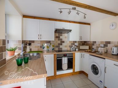 A kitchen with white cabinets a washing machine an oven a sink and wooden countertops at Ammonite Cottage in Fortuneswell Portland