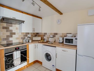 A kitchen with white cabinets a washing machine a microwave kettle and refrigerator at Ammonite Cottage in Fortuneswell Portland