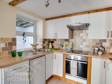 A kitchen with white cabinets dishwasher sink oven and countertop accessories at Ammonite Cottage Fortuneswell Portland