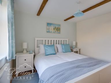 A bedroom with a white double bed blue pillows and a grey blanket at Ammonite Cottage in Fortuneswell Portland
