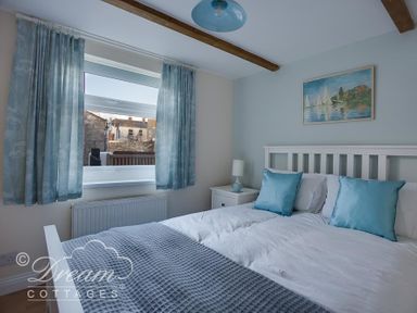 A bedroom with a white bed frame blue pillows bedside table with lamp and blue curtains at Ammonite Cottage Fortuneswell Portland